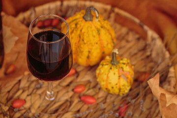 Glass of red wine on wooden table decorated with pumpkins and dried leaves outdoor. Autumn...