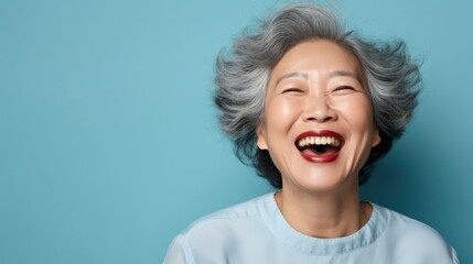 A mature Asian woman, isolated on a sky-blue background, her eyes twinkling with mischief, showcasing moments of playfulness.