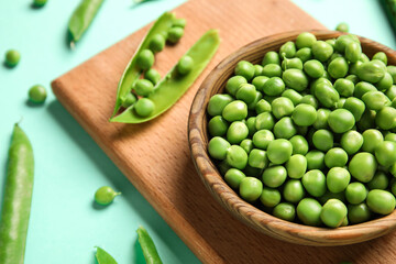 Bowl and wooden board with fresh green peas on turquoise background