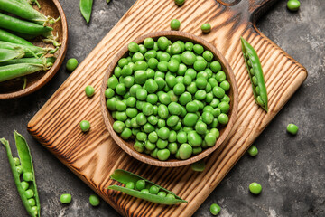 Bowls and wooden board with fresh green peas on black background