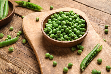 Bowl and board with fresh green peas on wooden background
