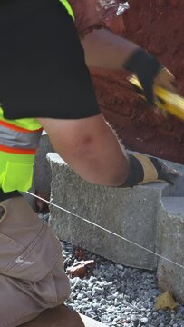 Construction worker lifted concrete block positioned it on retaining wall.