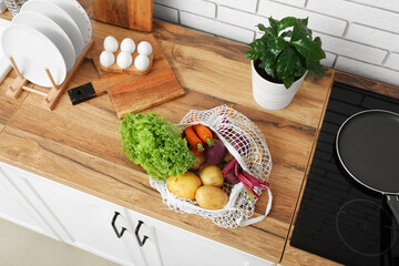 Mesh bag with different fresh vegetables on counter in kitchen