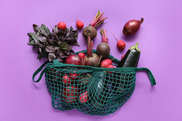 Mesh bag with different fresh vegetables on purple background