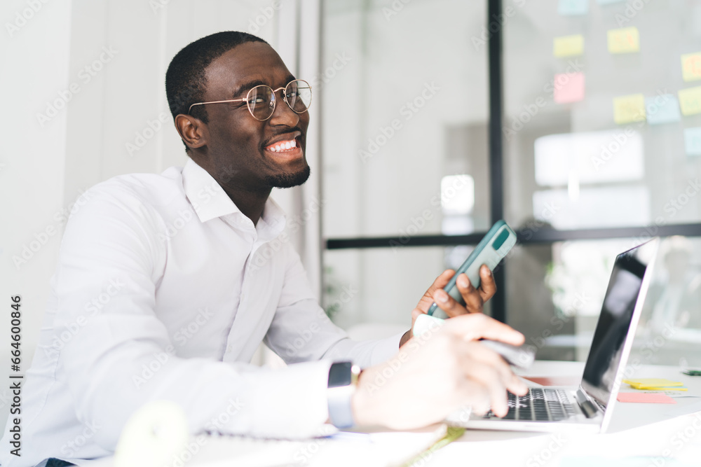 Poster man talking on smartphone while working on laptop in office