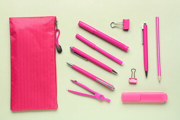 Pink pencil case with school stationery on green background