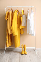 Fototapeta premium Rack with stylish clothes and rubber boots near color wall