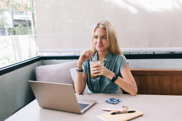 Carefree female blogger with digital netbook technology smiling during free time for remote working...