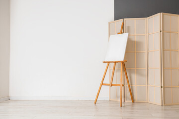Wooden easel with blank canvas near white wall