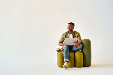 Smiling african american man sitting on green design chair with portable laptop on knees over white background with copy space.