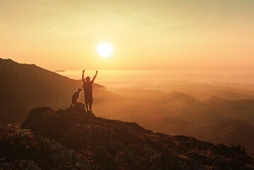 silhouette of a mountaineer man raising his arms and contemplating the sunset after hiking in the...