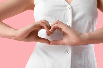 Young woman with healthy stomach making heart gesture on pink background, closeup