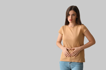 Young woman suffering from stomach ache on light background - obrazy, fototapety, plakaty