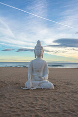 Statue of Buddha in the full lotus seated meditation posture on a beach on sunrise in Spain
