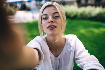 Close up selfie portrait of attractive female posing during summer daytime in park keeping travel lifestyle, charming Caucasian woman looking at camera during leisure for creating influence content