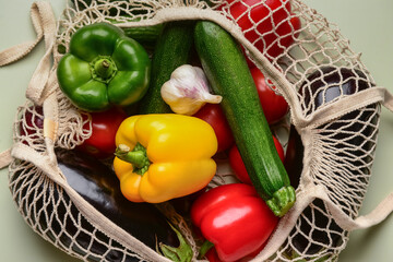 Mesh bag with different fresh vegetables on light green background