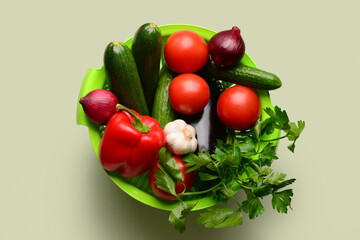 Colander with fresh vegetables and greenery on light green background