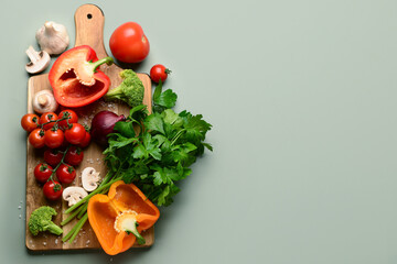 Wooden board with fresh vegetables and greenery on grey background
