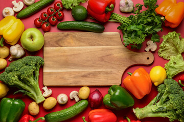 Wooden board with fresh vegetables, fruits and mushrooms on red background