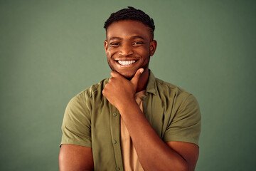 New ideas and thoughts. Portrait of smiling african american man keeping hand near chin and looking at camera over green background. Thoughtful guy in khaki shirt searching for inspiration in studio. - obrazy, fototapety, plakaty