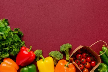 Poster Paper bag with tomatoes and fresh vegetables on burgundy background © Pixel-Shot