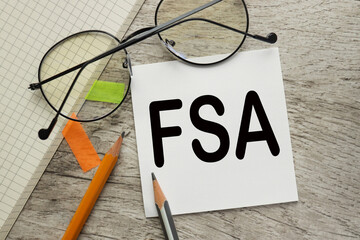 FSA - Flexible Spending Account. text on white paper for writing. on a yellow notepad.