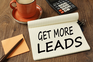 orange sticker, orange mug on wooden table, notepad with text Get More Leads