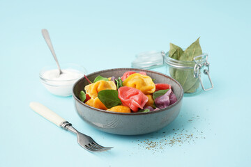 Bowl with boiled colorful dumplings and spinach on blue background