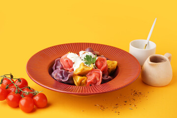 Plate of boiled colorful dumplings with sour cream and parsley on orange background