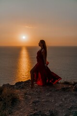 Woman sunset sea red dress, back view a happy beautiful sensual woman in a red long dress posing on a rock high above the sea on sunset.