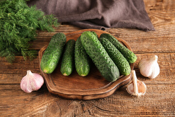 Board with fresh cucumbers and garlic on wooden background