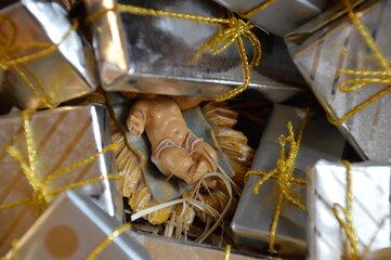 Jesus the baby in the manger hidden under a pile of presents as critical symbol for our excessive...