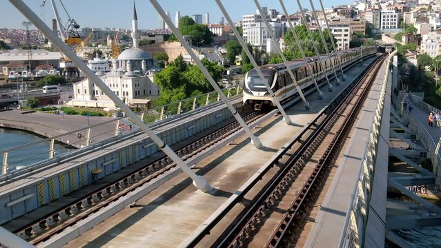 Subway train arriving to station located on cable-stayed metro bridge. Elevated subway train. Metro train arrives to Halic metro station on a bridge over Golden Horn bay, Istanbul, Turkiye