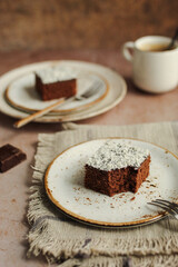 Easy chocolate and coconut cake. Rustic napkin and brown background. Cup of coffee.