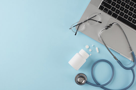 Transform your healthcare experience with virtual doctor appointments. Top view photo of laptop, stethoscope, eyewear, bottle with tablets on light blue background with advert zone