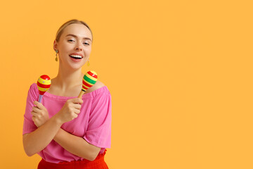 Pretty young woman with maracas on orange background