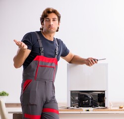 Young handsome contractor repairing fridge
