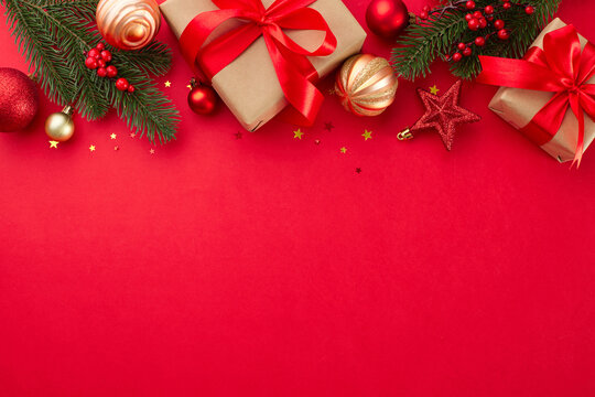 Explore the joy of holiday shopping for your loved ones. Top view photo of festive present boxes, holiday baubles, fir branches, shiny confetti on red background with promo zone