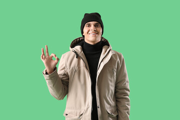 Young man in winter clothes showing OK on green background