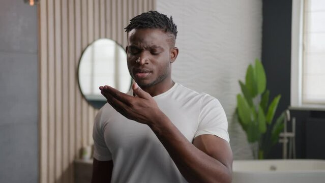 African American sad man with bad stink smell not fresh breathing applying breath spray freshener oral hygiene of mouth confident smiling male guy using dental care cosmetic product at home bathroom