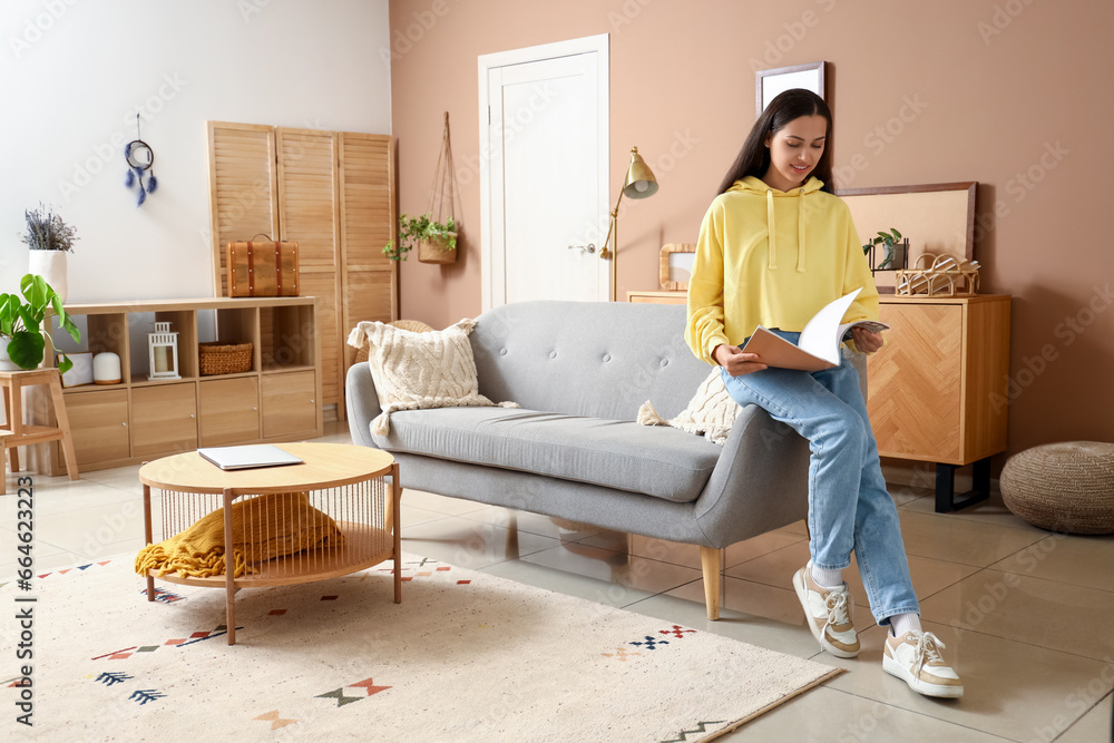 Wall mural Young woman in hoodie reading magazine at home