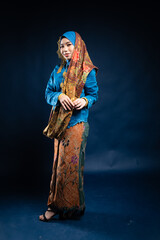 Muslim woman wearing traditional wear blue kebaya and hijab isolated on blue background. Idul Fitri and hijab fashion concept.