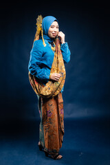 Muslim woman wearing traditional wear blue kebaya and hijab isolated on blue background. Idul Fitri and hijab fashion concept.
