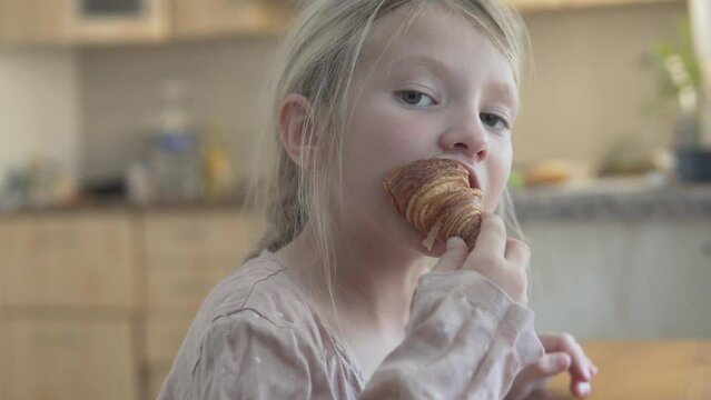 Beautiful little girl eating a bun in the morning in the kitchen