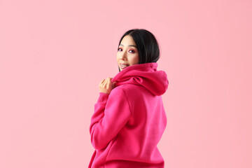 Young Asian woman in hoodie on pink background