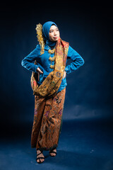 Muslim woman wearing traditional wear blue kebaya and hijab isolated on blue background. Idul Fitri and hijab fashion concept.