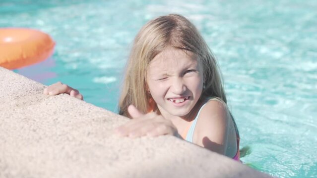 Close-up, beautiful little girl squinting in the pool from the bright sun in summer