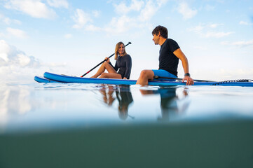 Young man and woman on the sea with a paddle surf board - obrazy, fototapety, plakaty