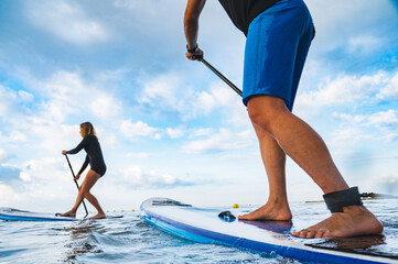 Feet of a man on top of a paddle surfboard - obrazy, fototapety, plakaty