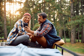 Happy couple of campers using smart phone while relaxing in nature.